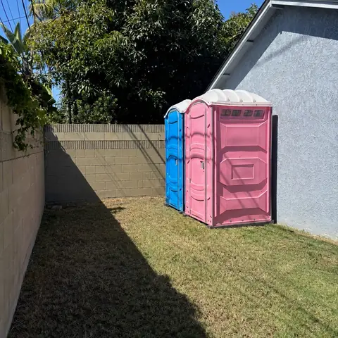 Pink and blue porta potties at the edge of a backyard