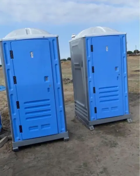 Blue and gray standard porta potties on a dirt job site