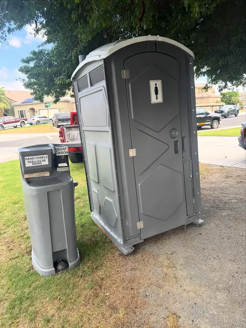 Gray standard porta potty with a hand-wash station on grass
