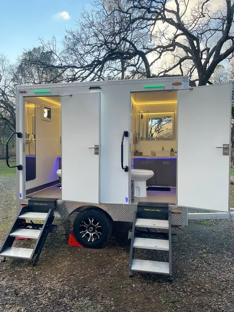 Two-stall restroom trailer with lit doors and fold-down steps