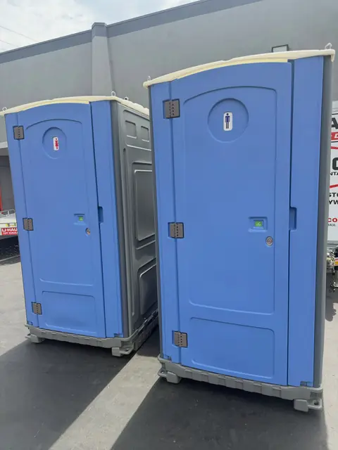 Two blue standard porta potties delivered side by side on pavement